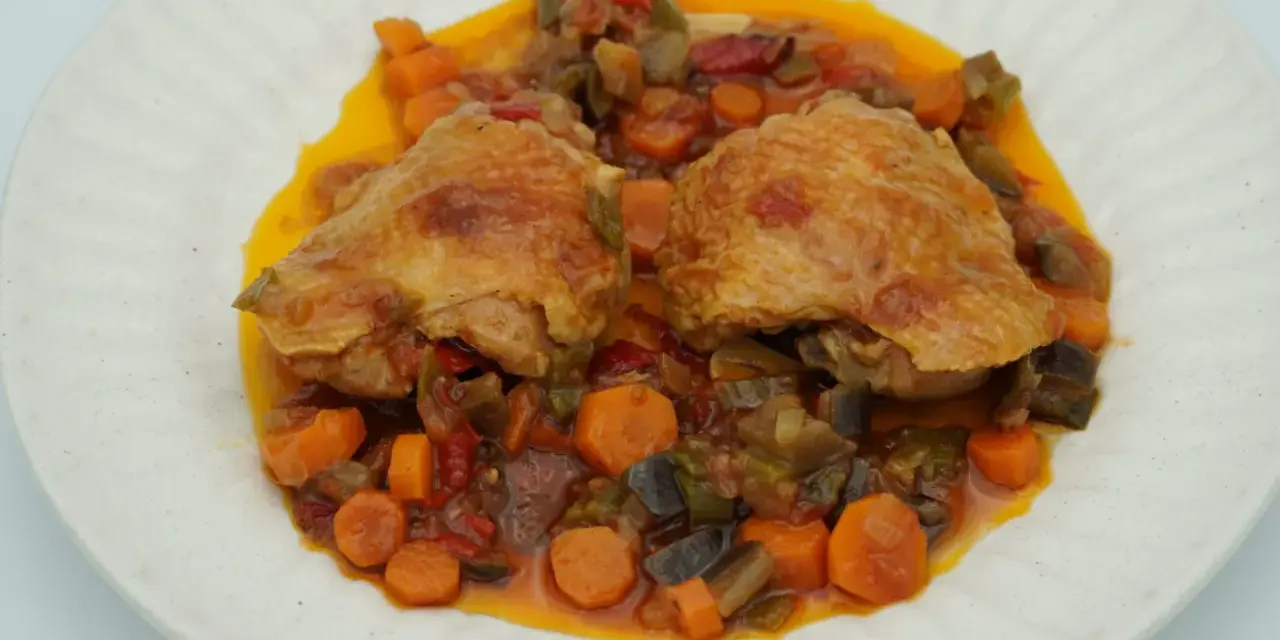 Dos piezas de pollo dorado sobre un guiso de verduras coloridas, zanahorias y berenjenas. Un delicioso pollo a la jardinera.