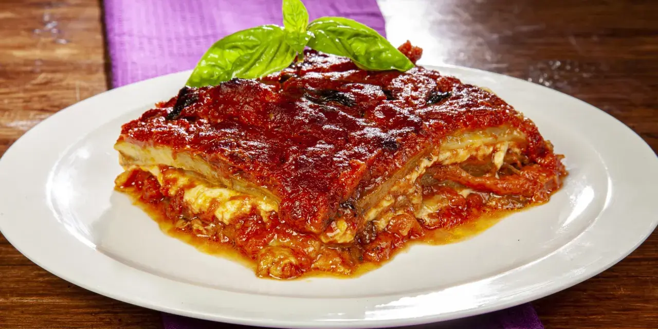 Una fetta di parmigiana di melanzane napoletana, ricca e saporita, guarnita con basilico fresco.