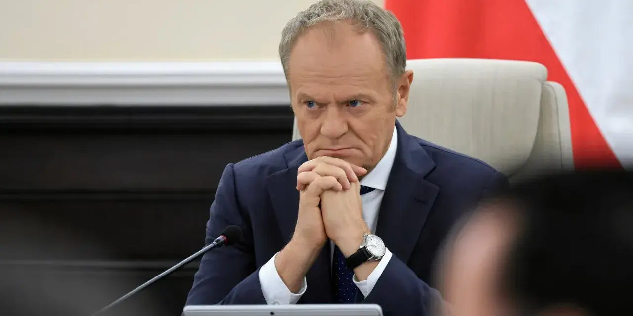 Mężczyzna w garniturze, z zaciętą miną, wygląda jak pesymista. Dłonie splecione, wzrok utkwiony w dal.
