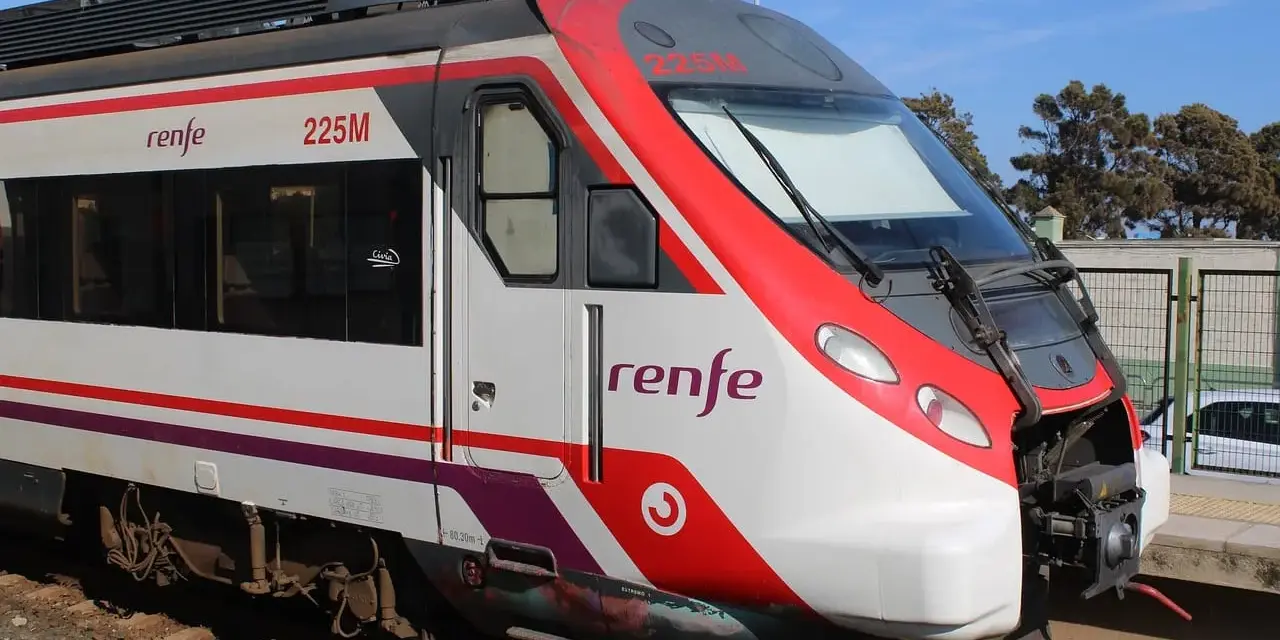 Czoło pociągu Renfe 225M z czerwonymi i białymi pasami, stojącego na torach.