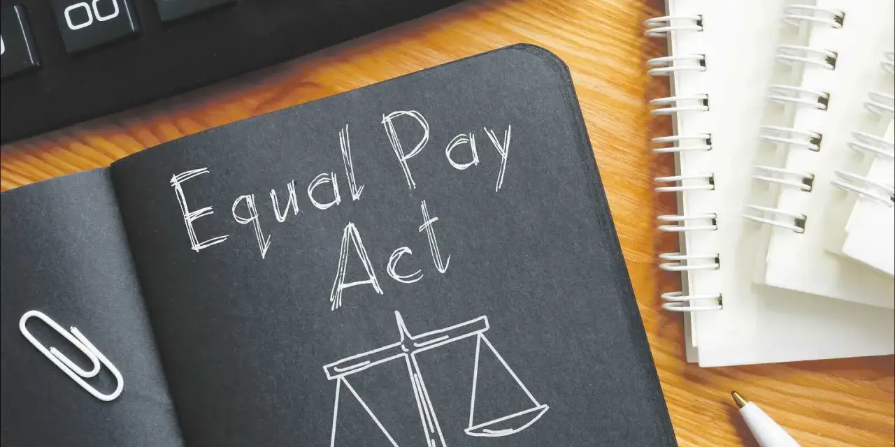 Notatnik z napisem "Equal Pay Act" i wagą sprawiedliwości symbolizuje jawność wynagrodzeń. Obok kalkulator i długopis.