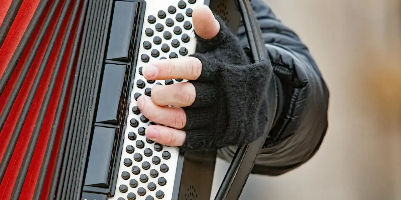 Dłoń w rękawiczce gra na akordeonie, wydobywając dźwięki tego wyjątkowego instrumentu.