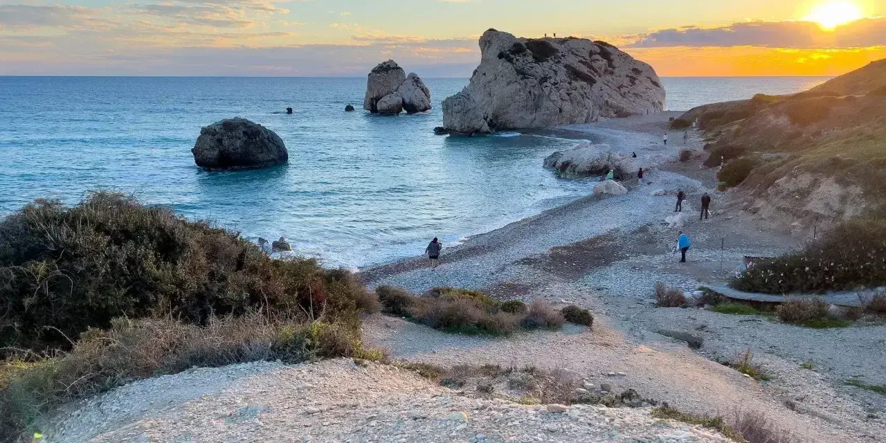 Piękna plaża na Cyprze w grudniu. Pogoda łagodna, słońce zachodzi nad morzem, a ludzie spacerują po kamienistym brzegu.