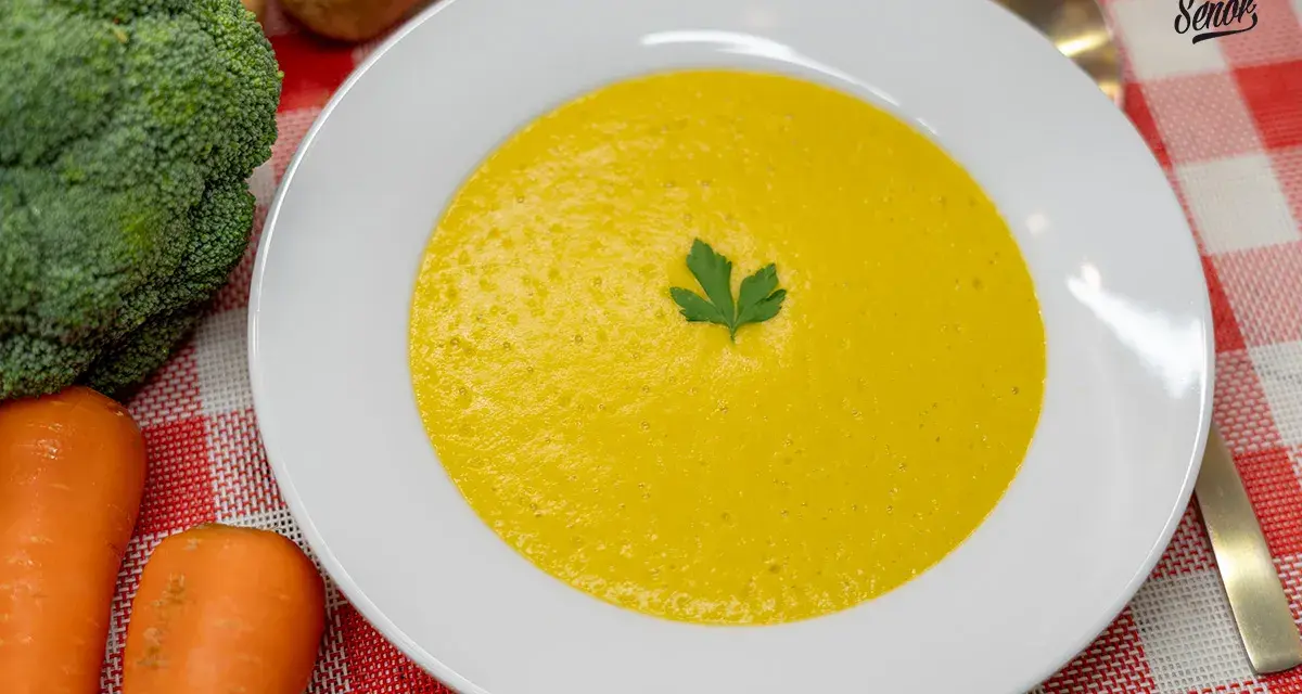 Un cremoso puré de verduras, con brócoli y zanahorias frescos al lado, listo para disfrutar.
