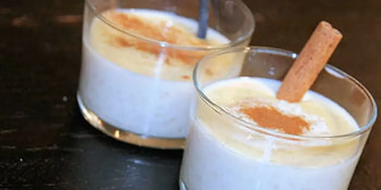 Deux verres de riz au lait crémeux, saupoudrés de cannelle. Un bâton de cannelle décore l'un des desserts, parfait pour une recette de riz au lait.