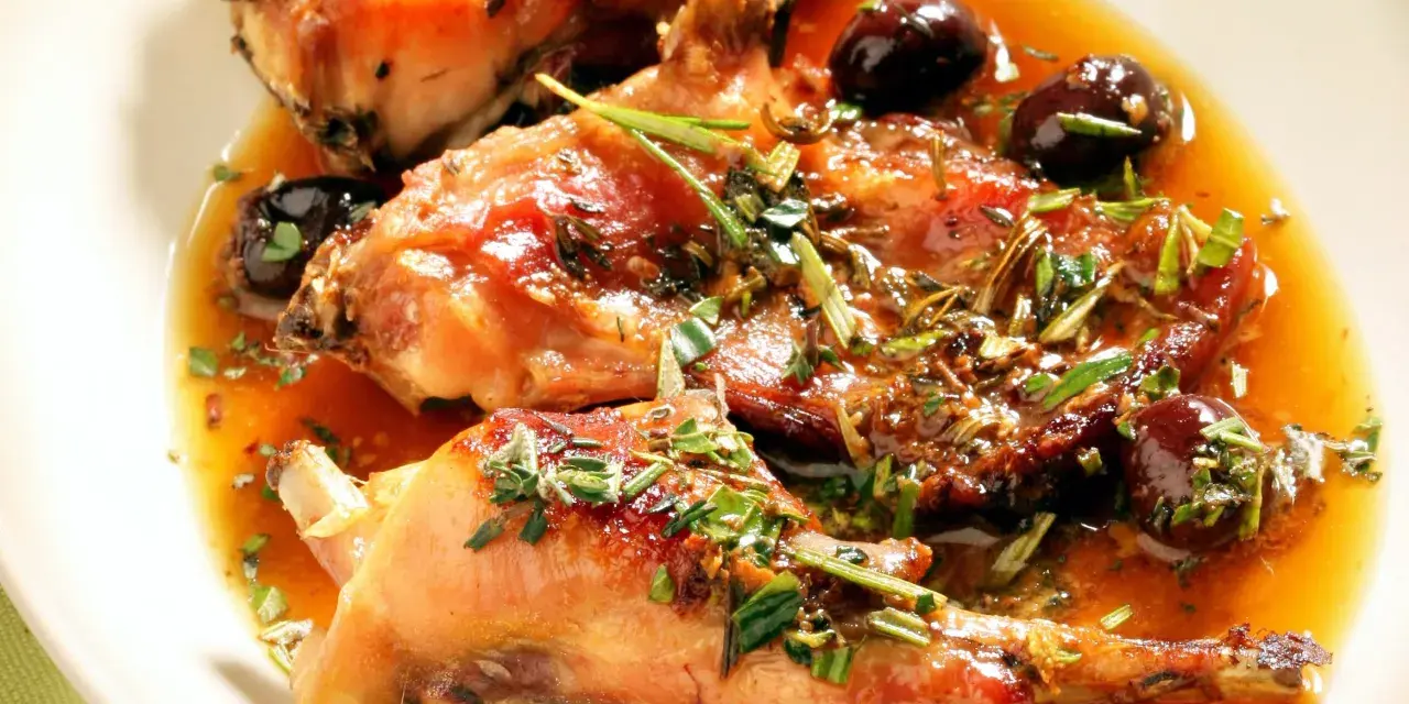 Coniglio alla ligure succulento, con olive nere e erbe aromatiche, servito in un piatto bianco.