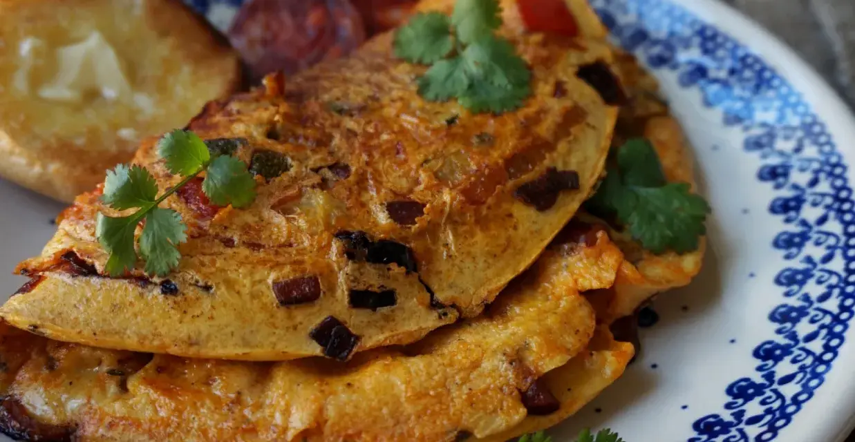 Pyszny omlet z chorizo, podany z grzankami i świeżą kolendrą, na talerzu z niebieskim wzorem.