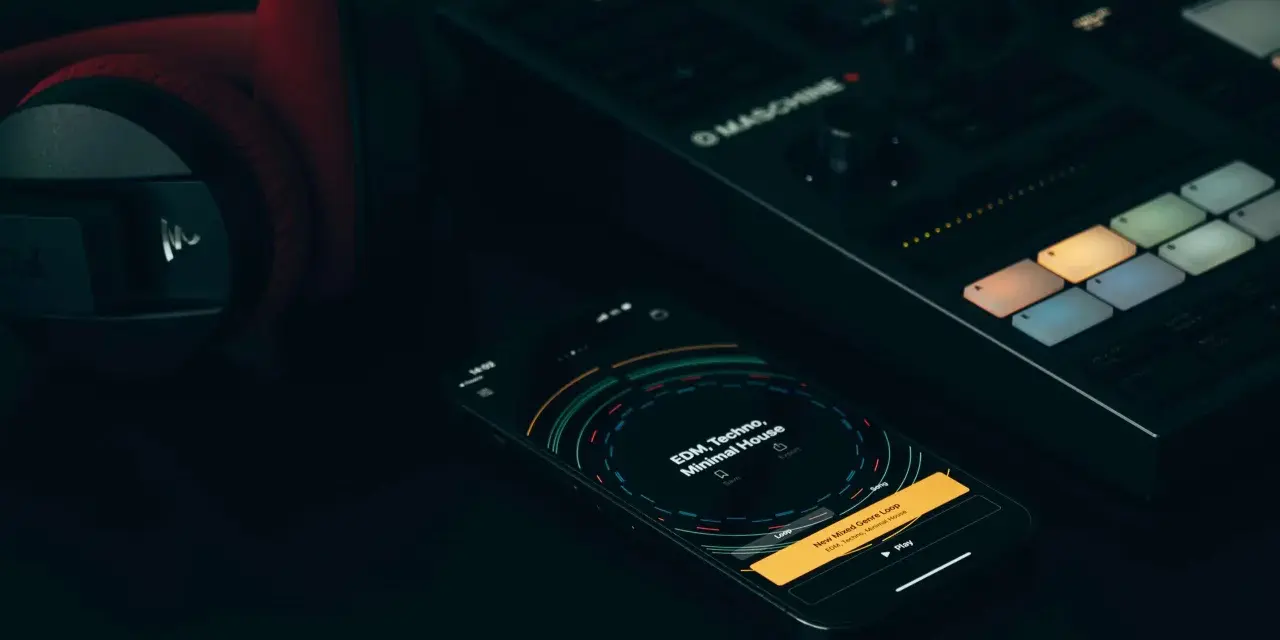 Czerwone słuchawki, kontroler Maschine i smartfon z aplikacją do tworzenia muzyki, gdzie widać koala sampler.