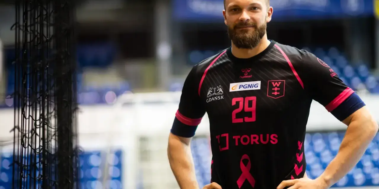 Piłkarz ręczny z numerem 29 na koszulce Torus Wybrzeże Gdańsk, z brodą, w czarnej koszulce z różowymi akcentami.