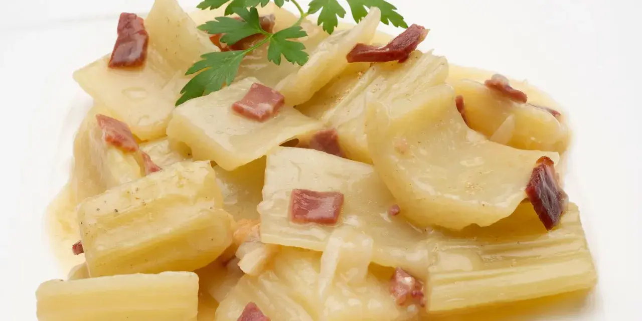 Cardo a la navarra, un plato tradicional con trozos tiernos de cardo en una cremosa salsa, adornado con trocitos de jamón y perejil fresco.