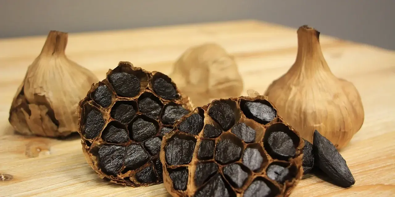 Ajos negros enteros y cortados, mostrando sus dientes oscuros y arrugados. Descubre las increíbles ajo negro propiedades.
