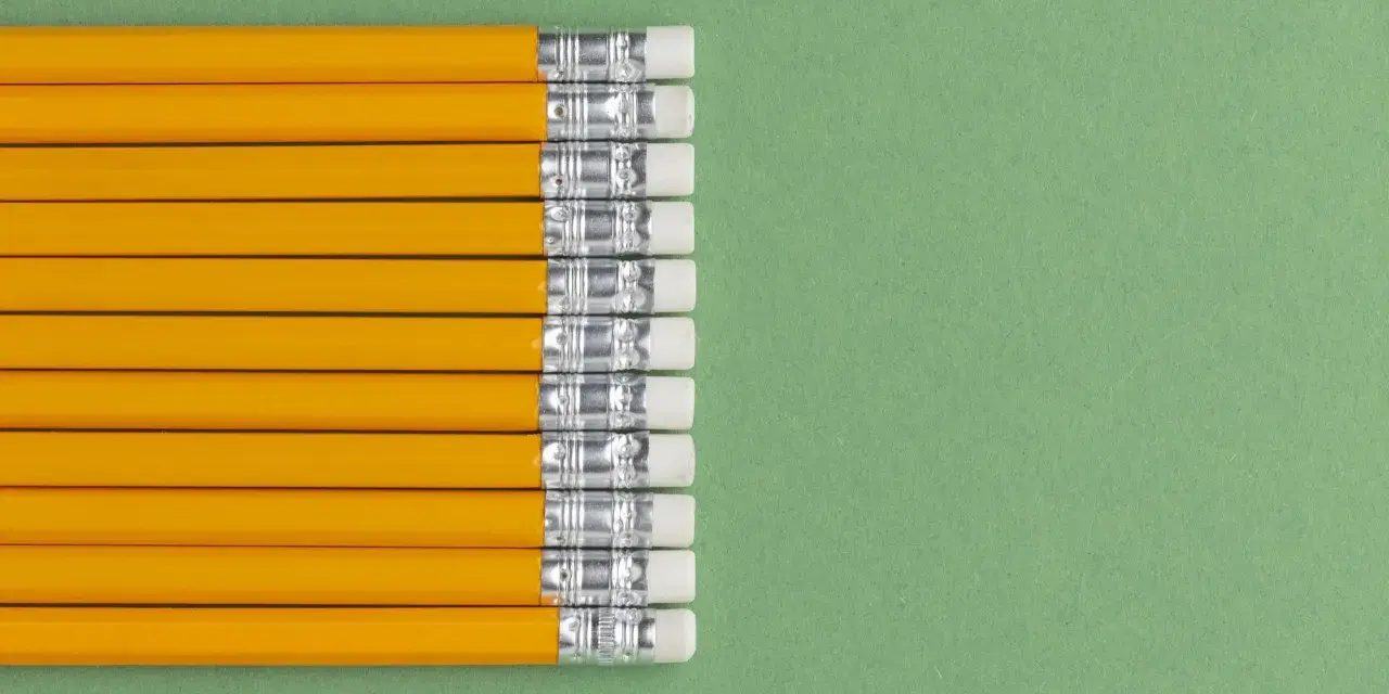Una fila de lapiceros o portaminas amarillos con gomas de borrar blancas sobre un fondo verde.
