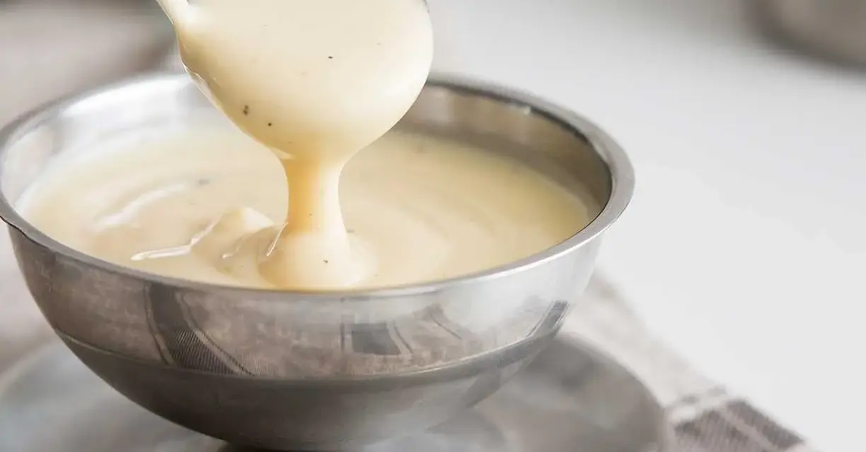 Krämig vaniljsås hälls upp ur en slev i en skål. Perfekt till efterrätt, här är ett enkelt vaniljsås recept.