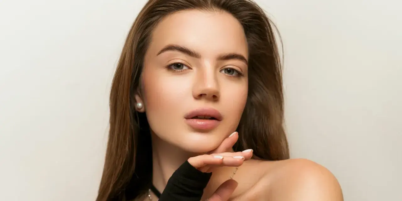 Delikatny makijaż nude podkreśla naturalne piękno młodej kobiety. Jej skóra lśni subtelnym blaskiem, a usta kuszą delikatnym kolorem.