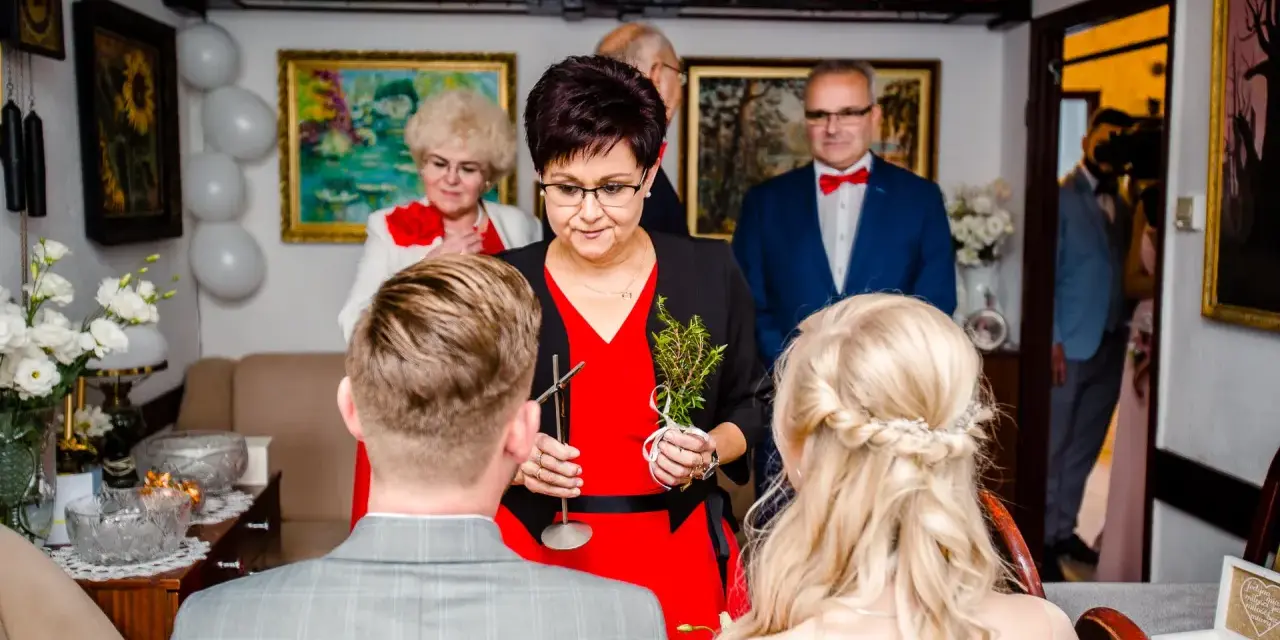 Tradycyjne błogosławieństwo pary młodej. Kobieta w czerwonej sukience trzyma gałązkę ziół, błogosławiąc narzeczonych.