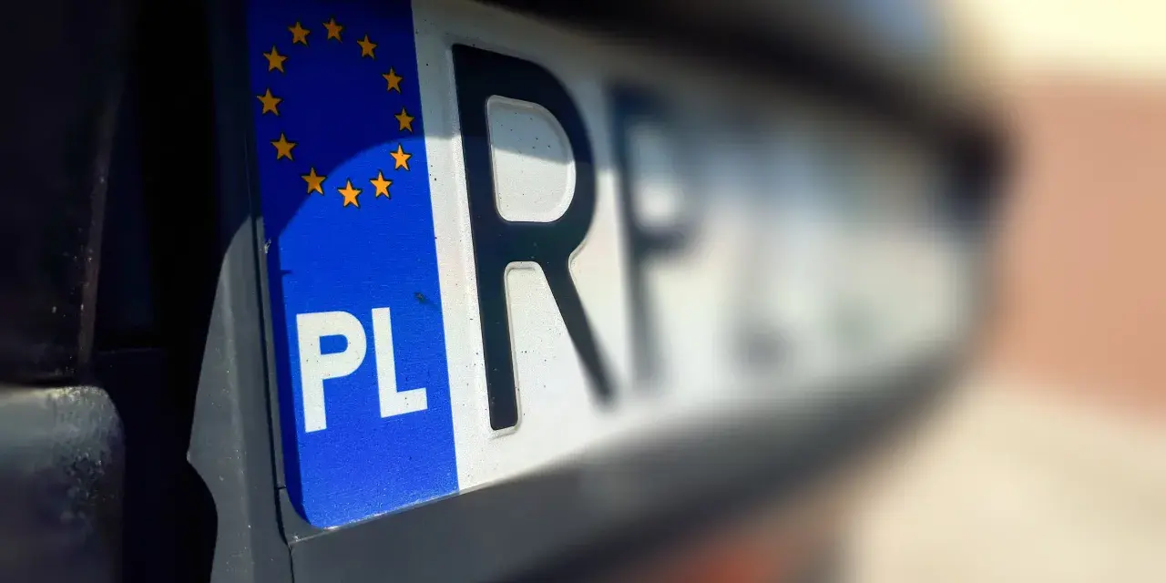 Zbliżenie na polską tablicę rejestracyjną z symbolem UE. Litery "PL" i fragment innych znaków sugerują, że pojazd jest w trakcie wyrejestrowania.