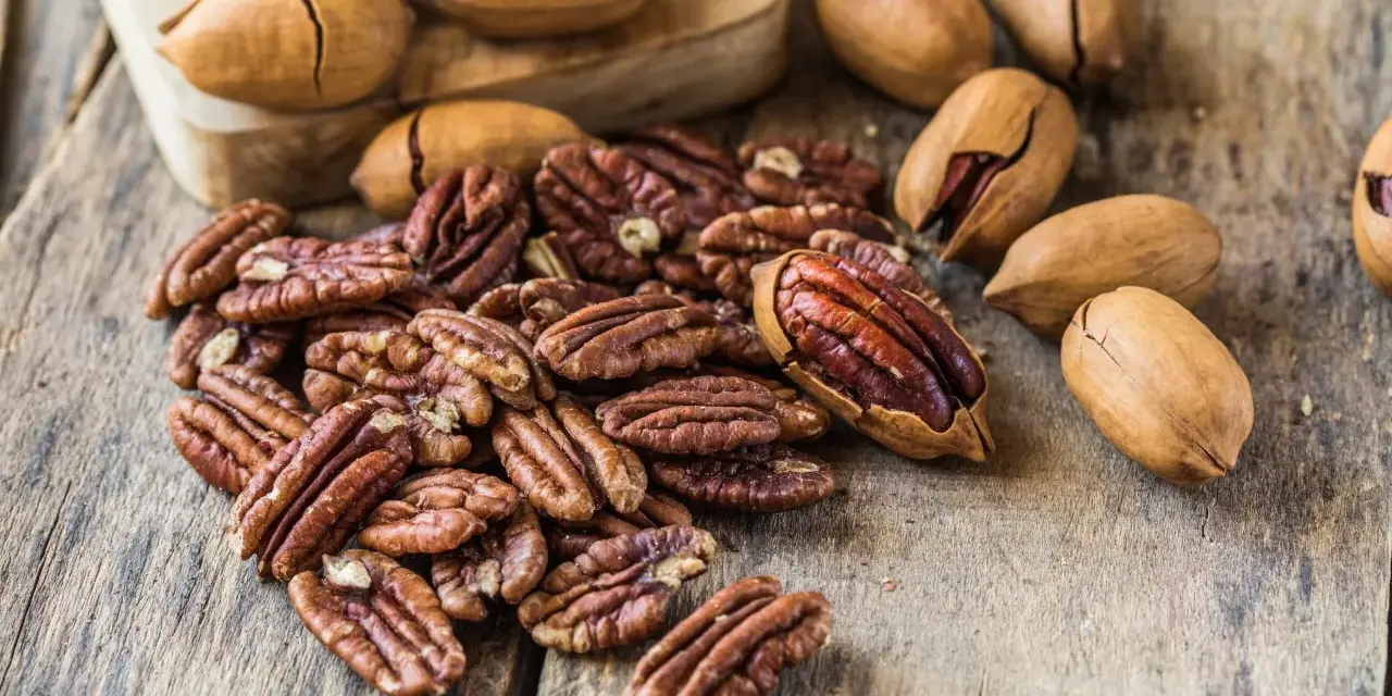 Noix de pécan décortiquées et entières sur fond de bois. Découvrez le noix de pécan bienfait pour une alimentation saine et gourmande.