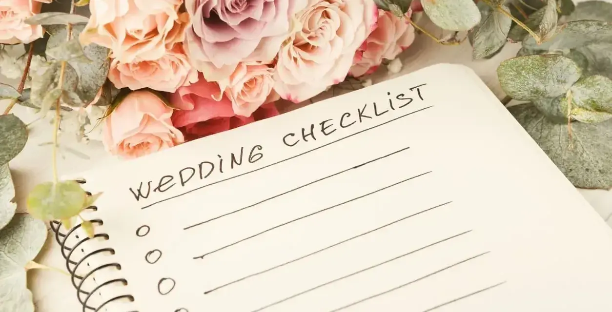 Bukiet róż i eukaliptusa obok notatnika z napisem "Wedding Checklist". Planowanie przebiegu wesela zaczyna się od listy zadań.