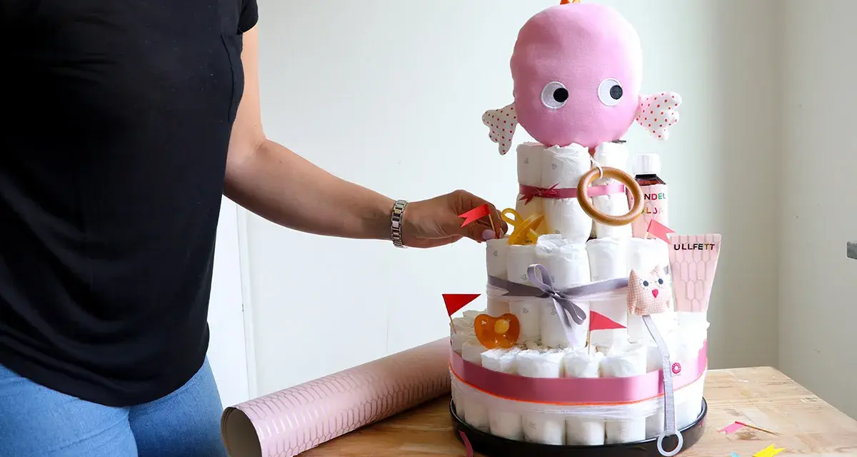En person lägger sista handen vid en blöjtårta dekoration med en rosa bläckfisk som topp.