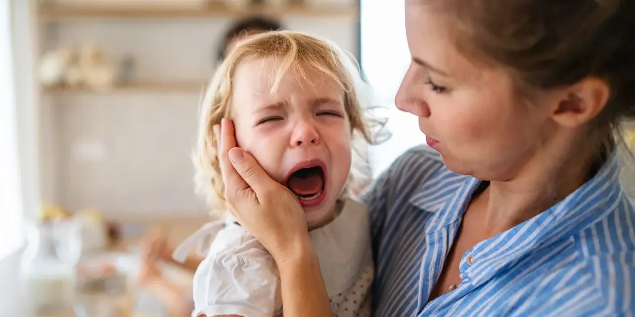Mama próbuje uspokoić płaczące dziecko, które przeżywa histerię. 5-latek krzyczy, a mama delikatnie trzyma go za policzek.