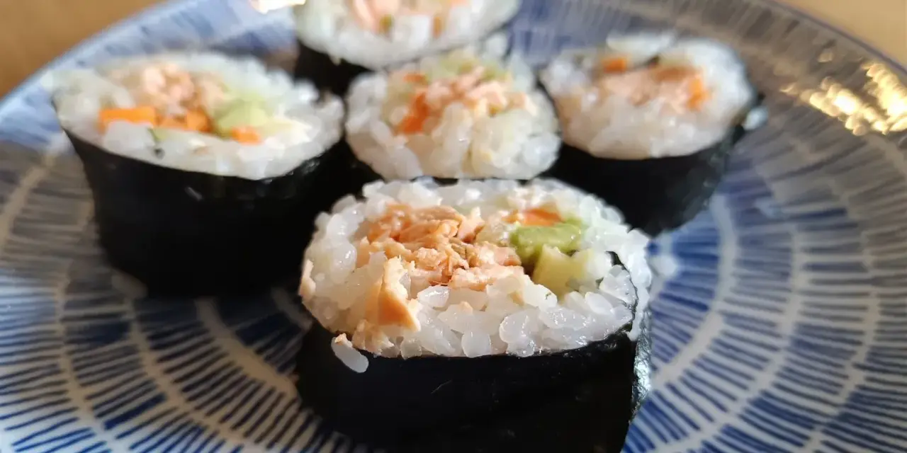 Pięć kawałków sushi z łososiem, ryżem i warzywami na niebiesko-białym talerzu.