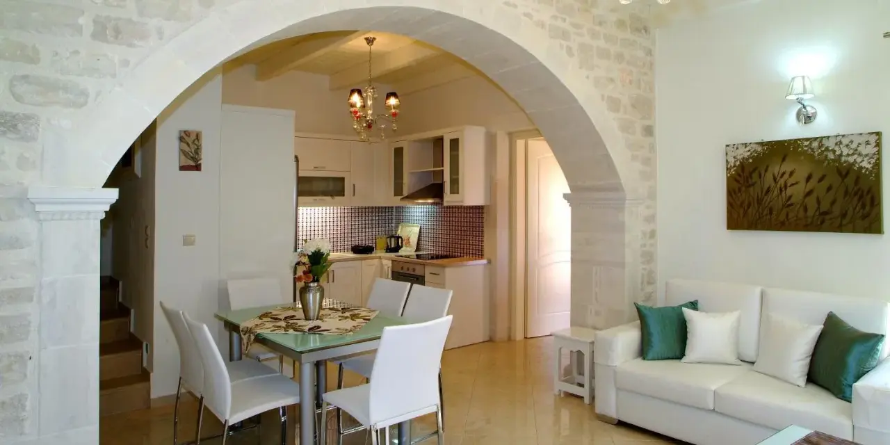 Un elegante soggiorno con un **arco in pietra moderno** che separa la zona pranzo dalla cucina. Divano bianco, quadri e lampadario di cristallo.