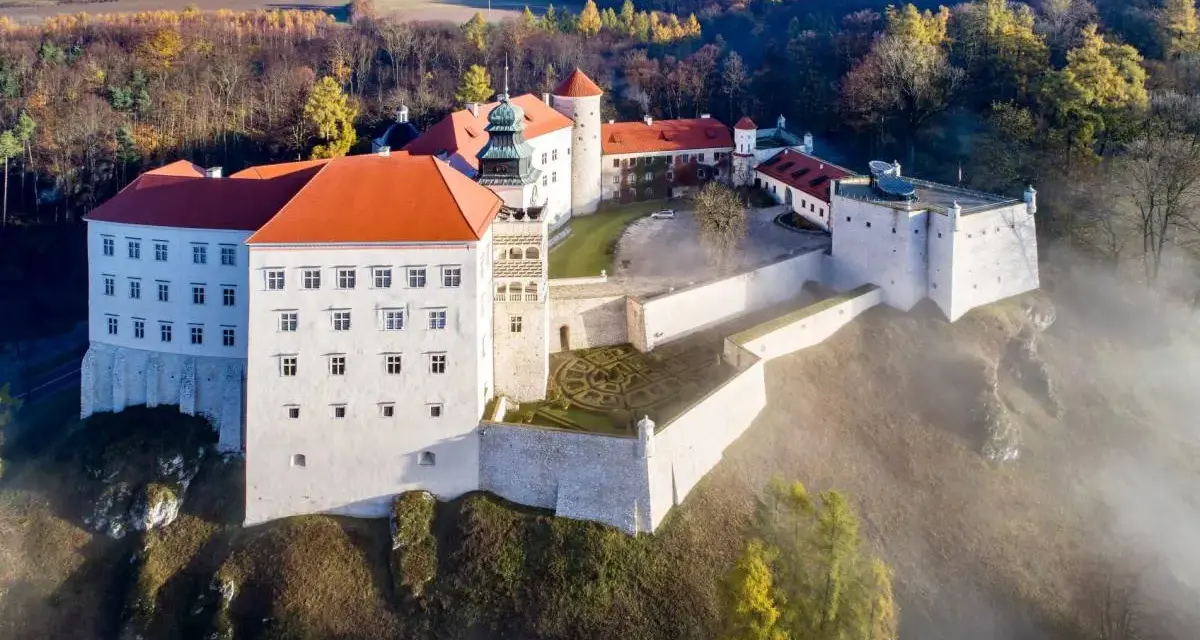 Majestatyczny zamek pod Krakowem, otoczony mgłą i jesiennym lasem, wznosi się na wzgórzu.