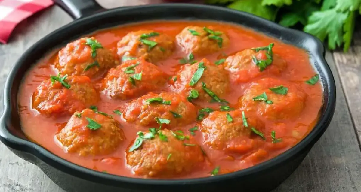 Polpette di lenticchie in salsa di pomodoro, guarnite con prezzemolo fresco, servite in una padella nera su un tavolo di legno.