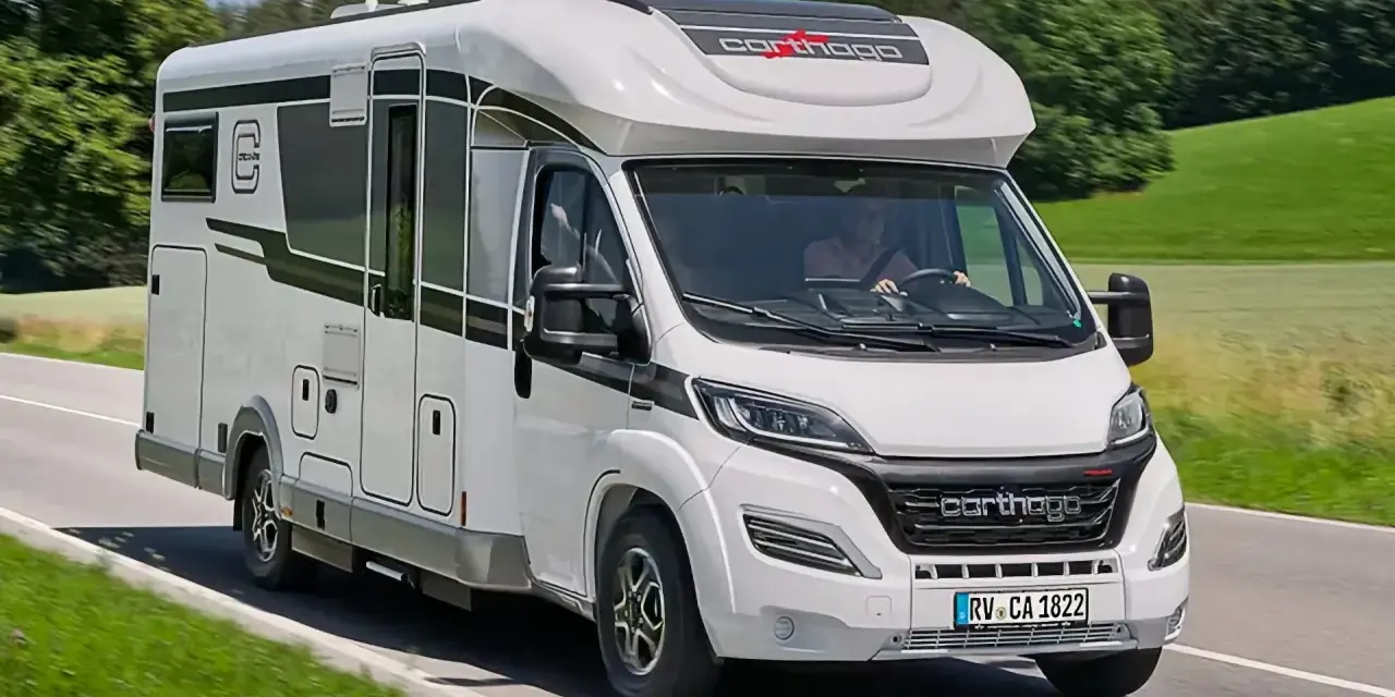 Biały kamper Carthago, największy kamper do 3,5 tony, jedzie po krętej drodze wśród zielonych wzgórz.
