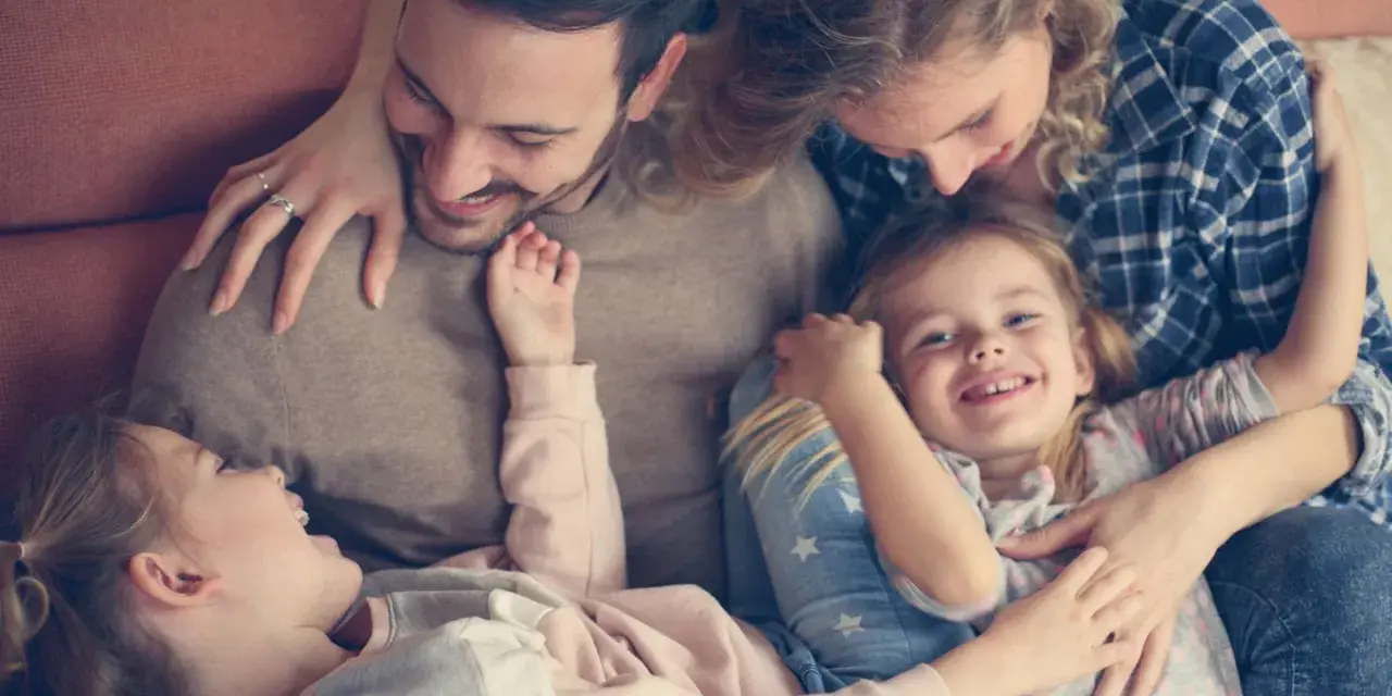 Glückliche Familie kuschelt auf dem Sofa. Zwei Elternteile umarmen ihre zwei Kinder, die sich an sie schmiegen.