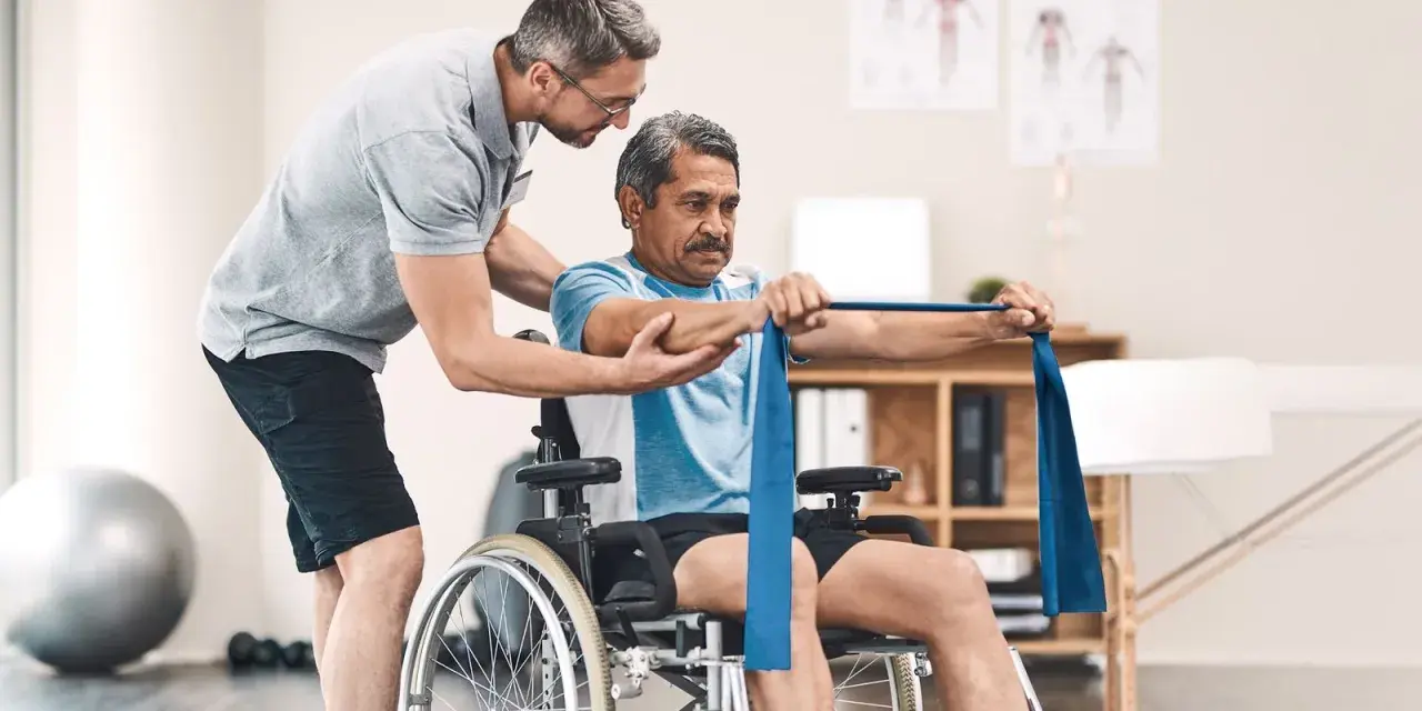 Ein Mann im Rollstuhl trainiert mit einem Therapeuten, der ihm hilft, die Widerstandsbandübungen auszuführen. Die Physiotherapeuten unterstützen ihn bei seiner Genesung.