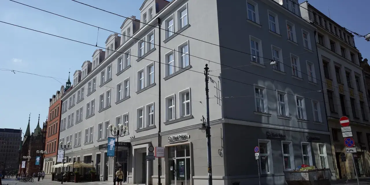 Elegancki hotel Korona Wrocław z szarym frontem i białymi oknami, na tle błękitnego nieba.