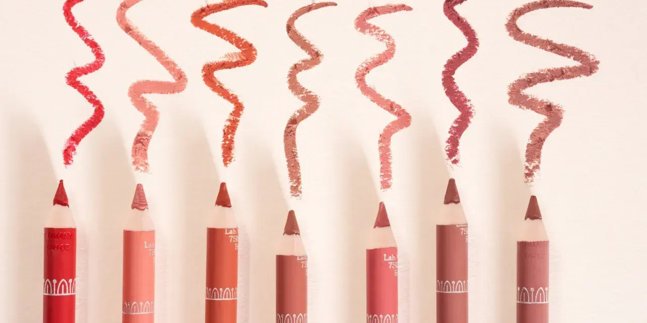 Plusieurs crayons à lèvres de différentes teintes, avec des échantillons de leur utilisation en traits ondulés.