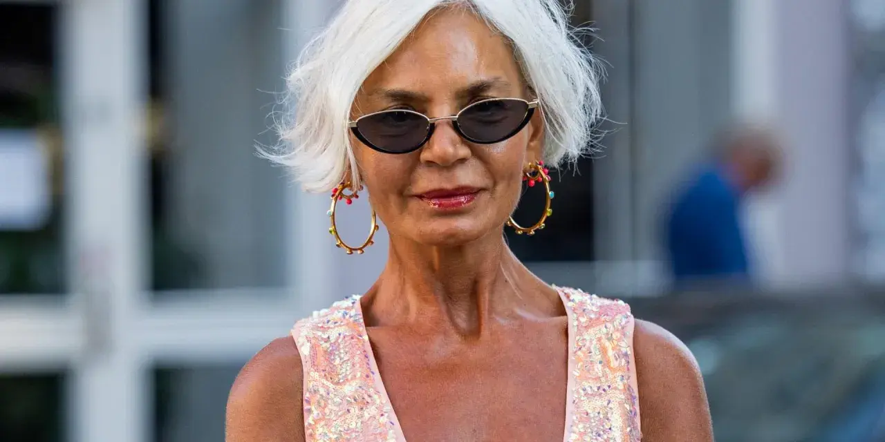 Frau mit weißem Kurzhaarschnitt, Sonnenbrille und auffälligem Schmuck.