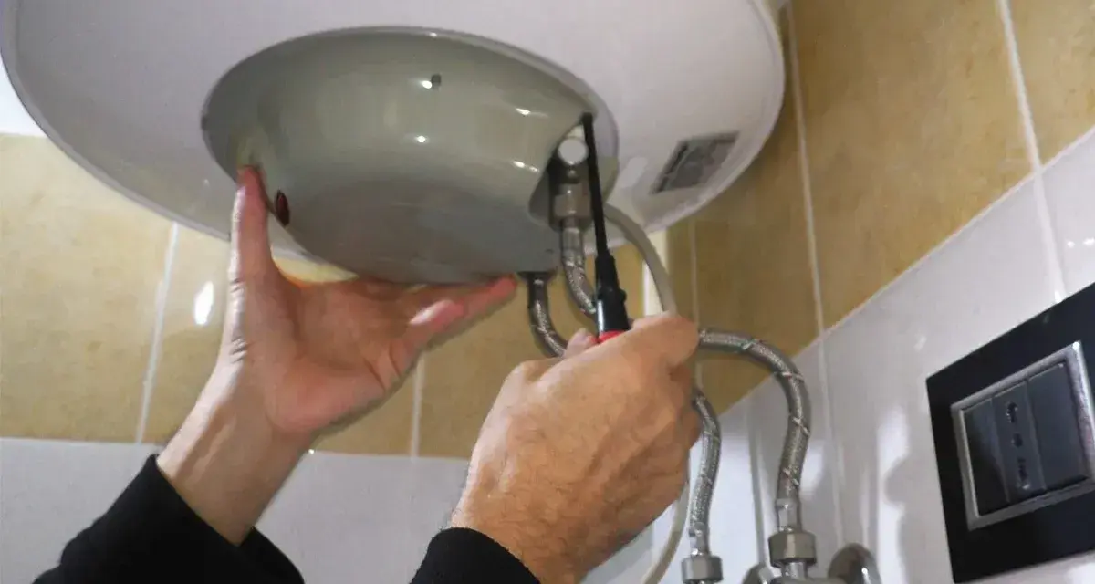 Mani che effettuano la manutenzione dello scaldabagno elettrico, avvitando una vite con un cacciavite.