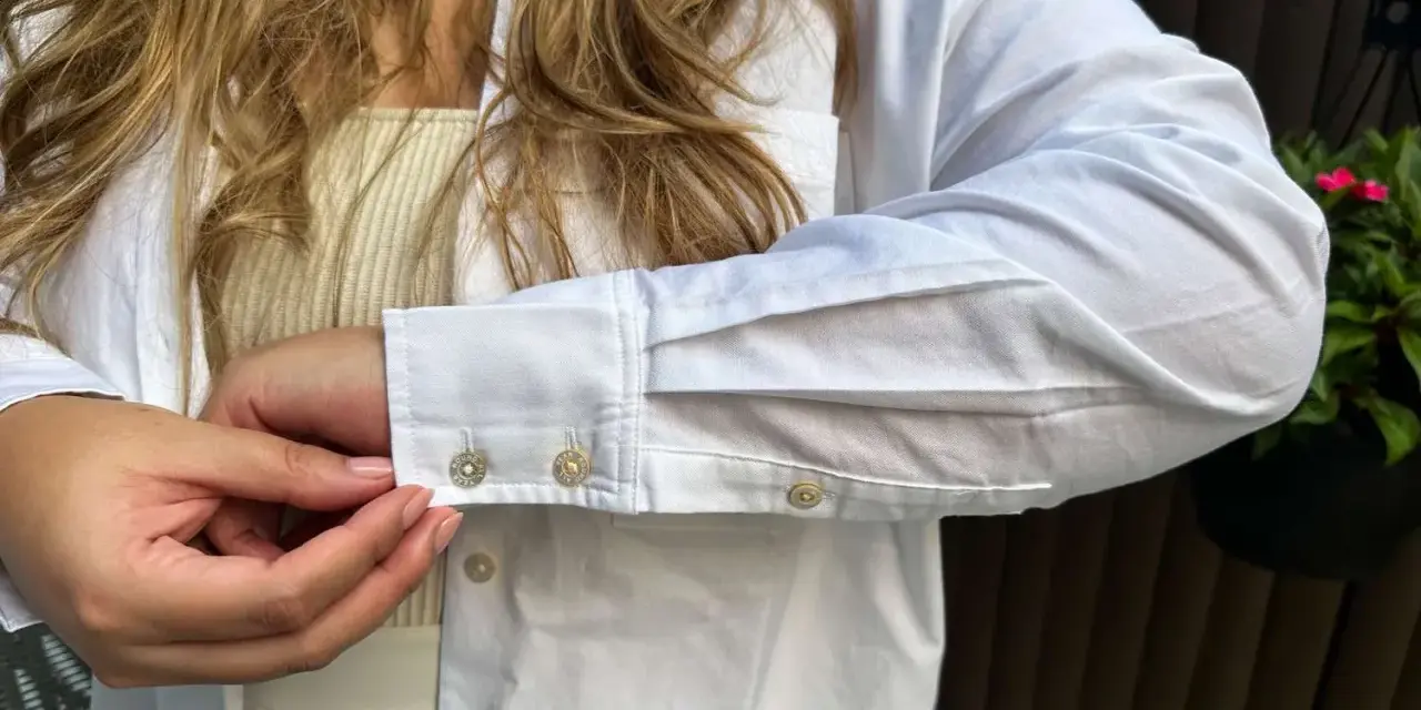 Sotto una camicia bianca, un top a coste color crema. Dettagli sui polsini con gemelli.