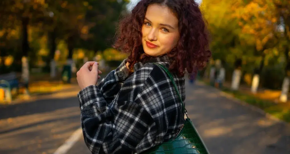 Dziewczyna w kratę, co to za styl? Ciepła flanela i zielona torebka na tle jesiennego parku.