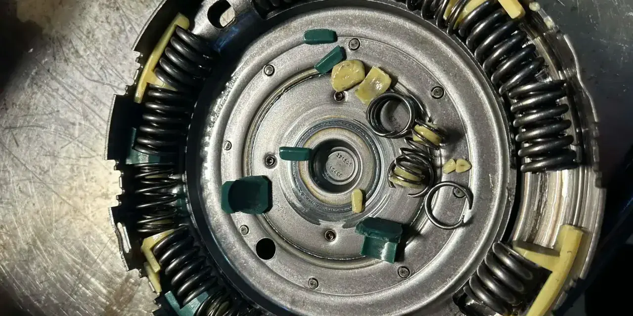 Zużyte elementy sprzęgła powershift: połamane zielone wkładki i sprężyny, objawy zużycia widoczne na metalowych częściach.