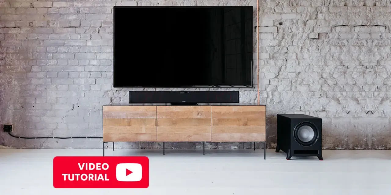 Schwarzer Subwoofer neben einem TV-Möbel. Hier erfahren Sie mehr über den subwoofer anschluss.