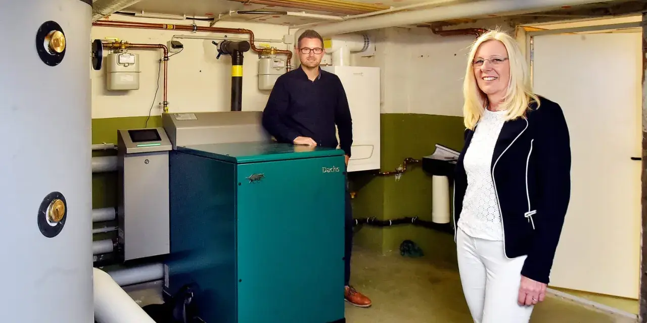 Mann und Frau stehen neben einem grünen Nano BHKW-Gerät in einem Heizungsraum.