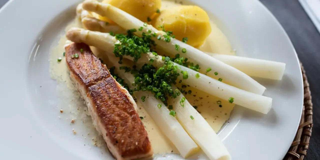 Ein Stück Lachs mit Spargel, Kartoffeln und Sauce Hollandaise. Der Spargel ist mit Schnittlauch bestreut.