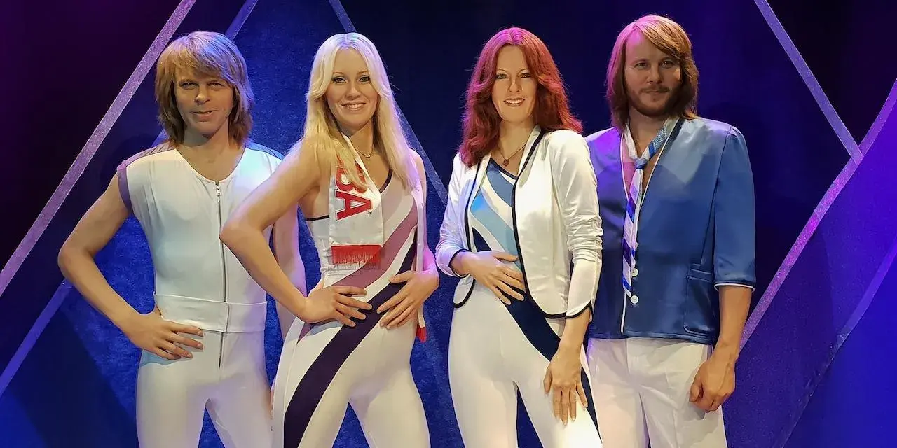 Les quatre membres du groupe suédois connu ABBA, figés dans leurs célèbres tenues colorées, posent devant un fond bleu et violet.