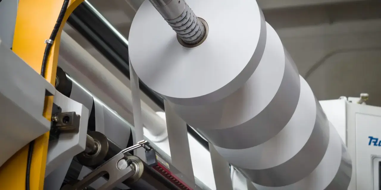 Rollo gigante de papel blanco en una máquina industrial. La densidad del papel es clave para la calidad de impresión.