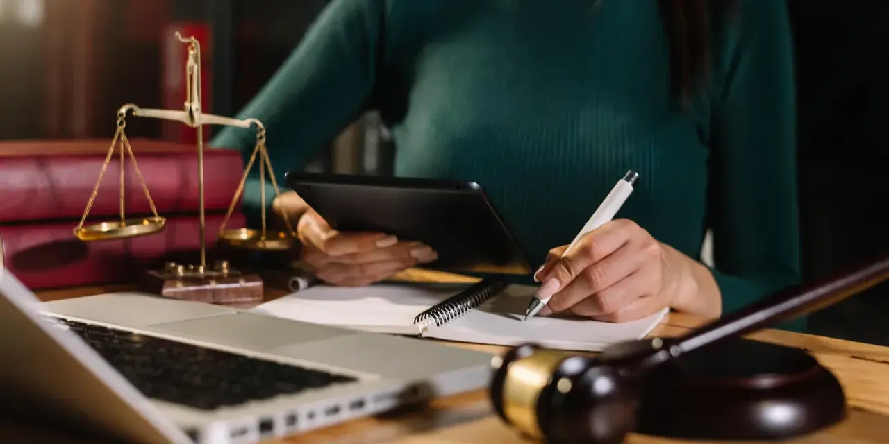Prawniczka analizuje dokumenty, pilnując, by nie przegapić ostatniego przedawnienia długu. Na biurku waga sprawiedliwości, laptop i młotek sędziowski.