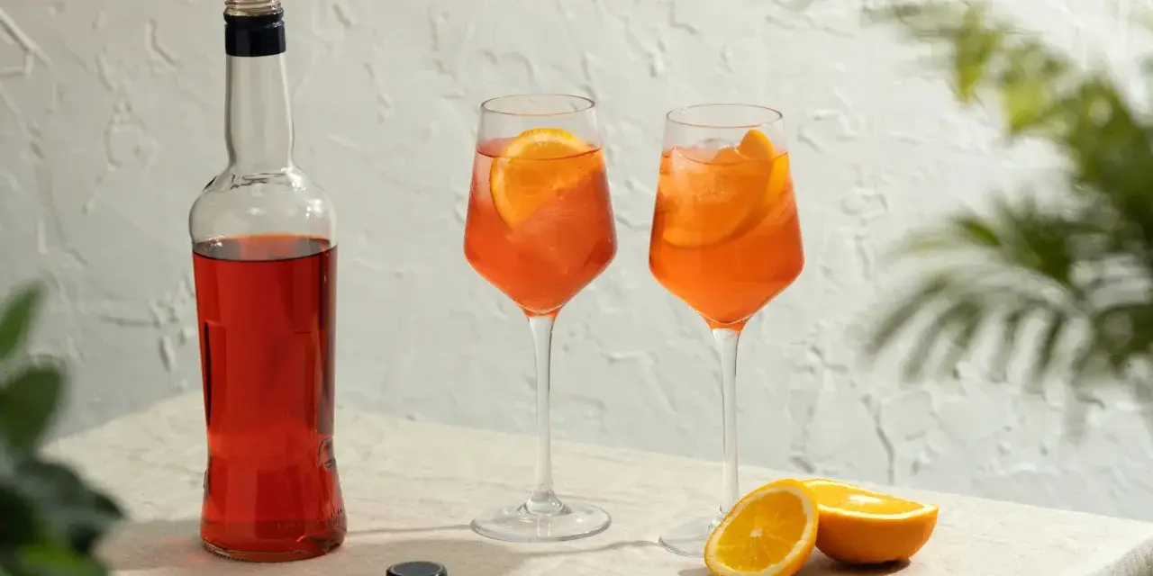Dwa orzeźwiające drinki aperol z colą, ozdobione plasterkami pomarańczy, stoją obok butelki aperolu.