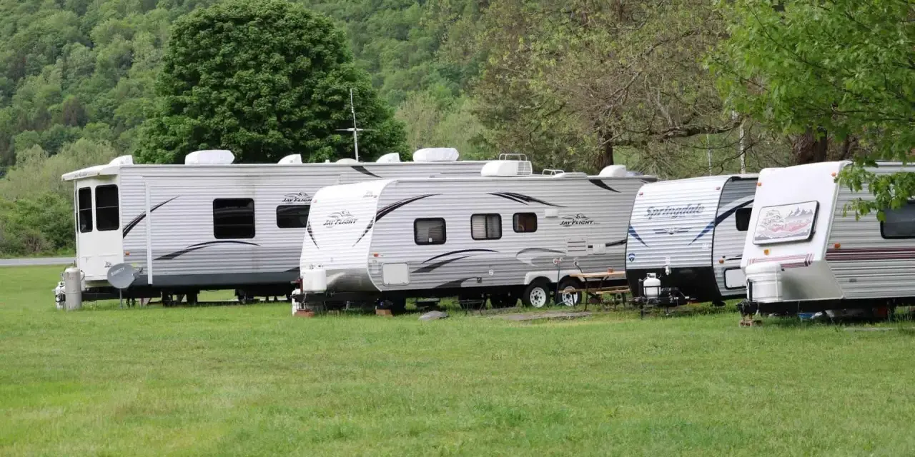 Rząd przyczep kempingowych na zielonej trawie, w tle las. Idealne miejsce na camping Górna Wetlinka.