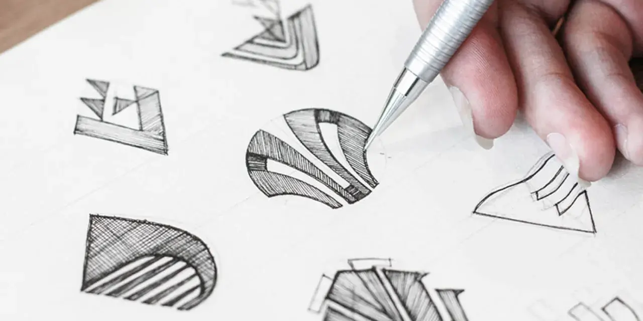 Main d'un designer esquissant des idées pour comment dessiner un logo. Plusieurs croquis abstraits sont visibles sur le papier.
