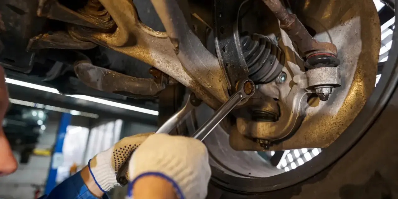 Mechanik dokręca śrubę w zawieszeniu samochodu. Widać elementy układu kierowniczego i amortyzator.