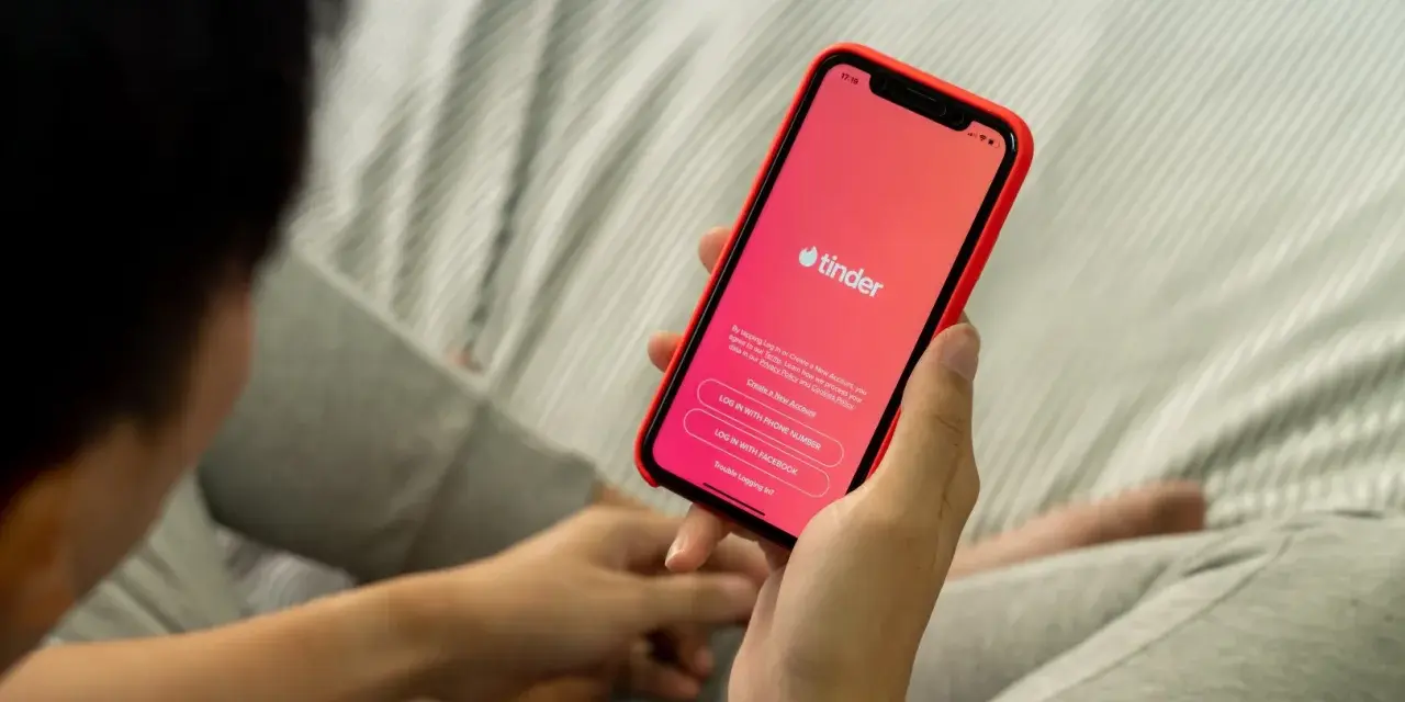Osoba trzyma telefon z aplikacją Tinder. Zastanawiasz się, czy warto założyć Tindera? Może to początek nowej znajomości.