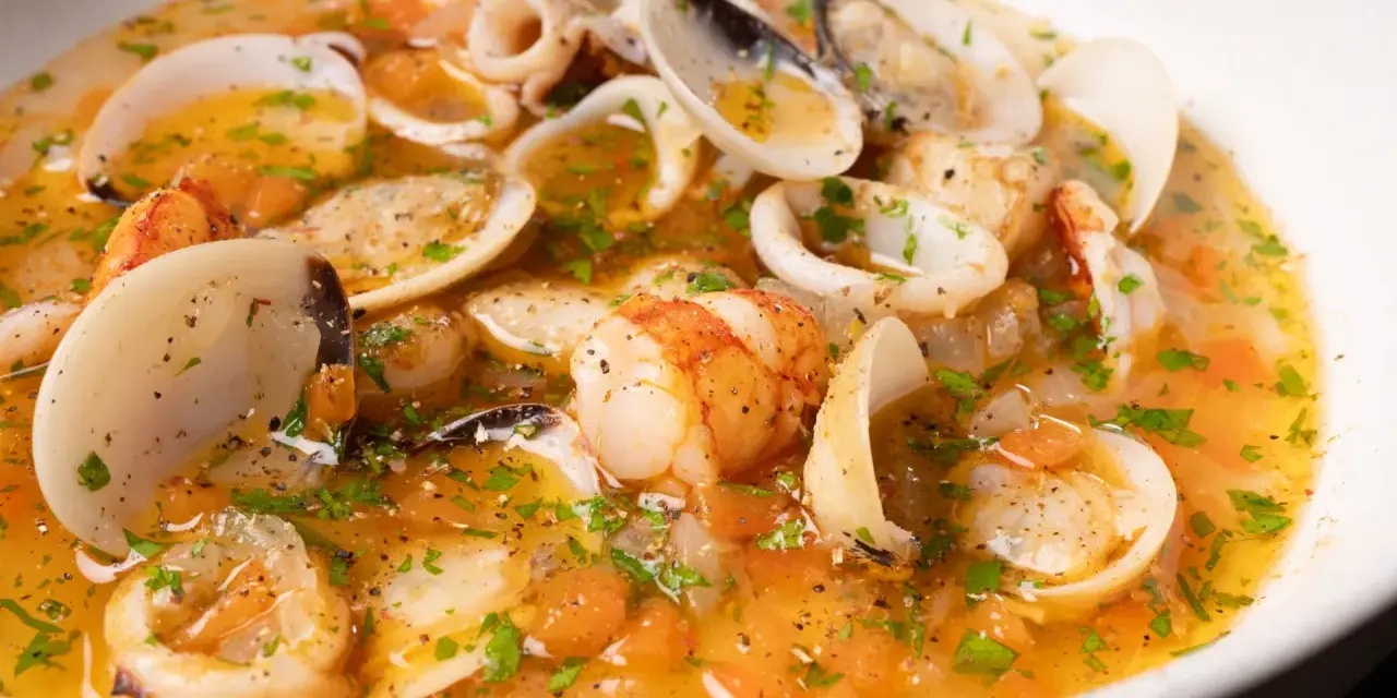 Sopa de mariscos con gambas, calamares y almejas en un caldo dorado con perejil.